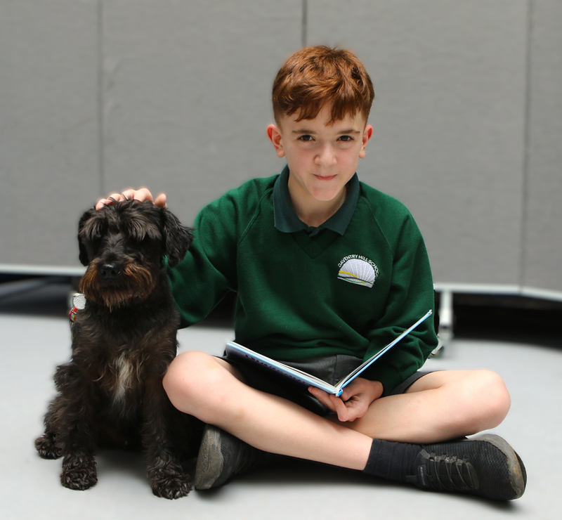 Boy reading a book with Raffie the school dog